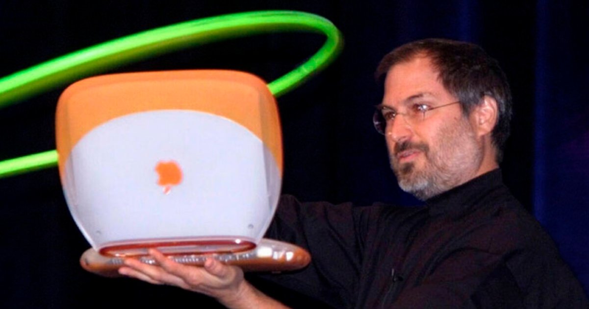 Steve Jobs holding an orange clamshell iBook